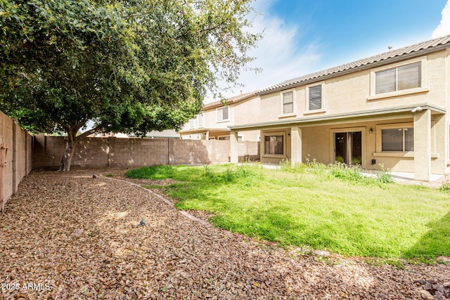 rear view of house featuring a yard, stucco siding, and a fenced backyard