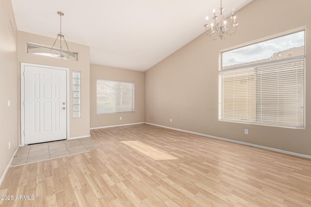 foyer entrance featuring a notable chandelier, light wood-style flooring, baseboards, and vaulted ceiling