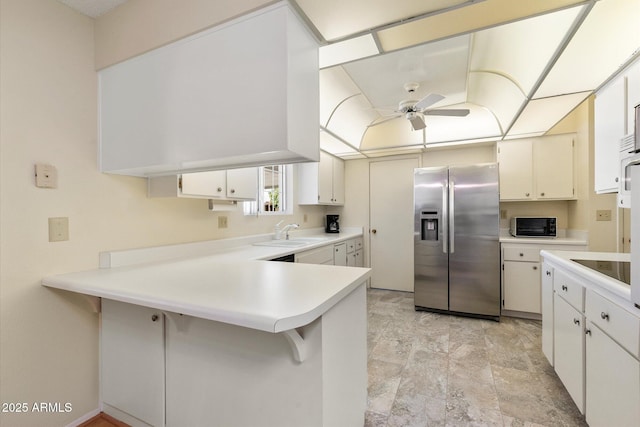 kitchen featuring black microwave, a peninsula, a sink, light countertops, and stainless steel refrigerator with ice dispenser