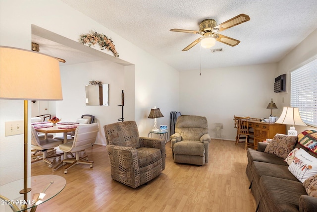 living room featuring light wood-style flooring, ceiling fan, and a textured ceiling