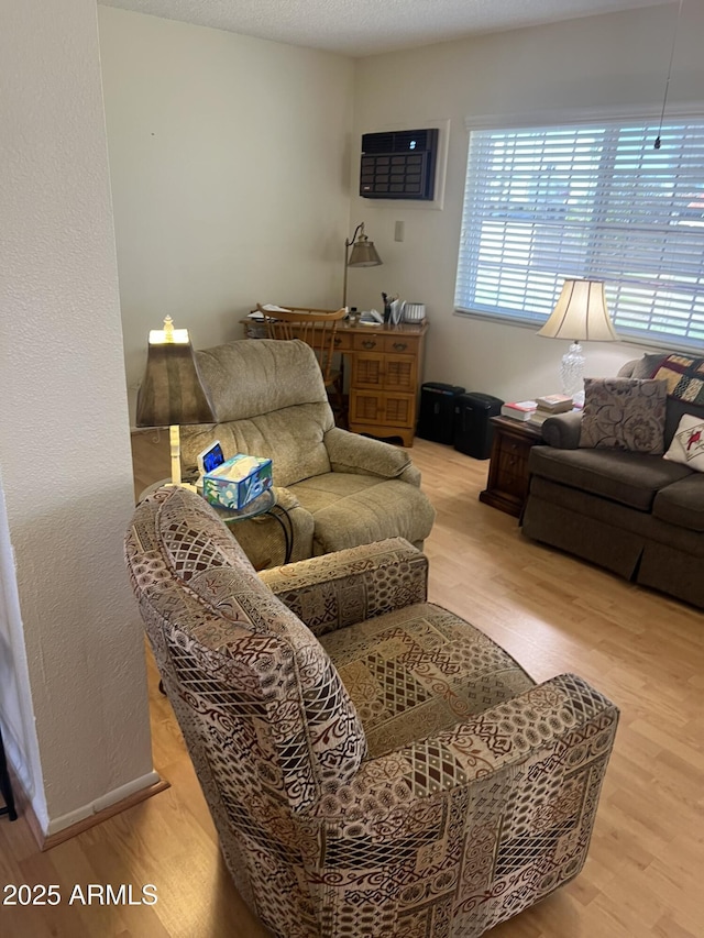 living area featuring an AC wall unit, a textured ceiling, baseboards, and wood finished floors