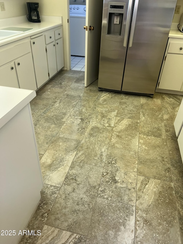 kitchen with a sink, white cabinetry, light countertops, stainless steel fridge, and washer / dryer