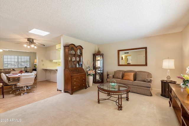 carpeted living area with a ceiling fan, a skylight, and a textured ceiling