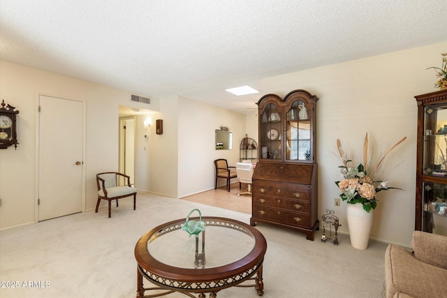 living area featuring carpet floors, a skylight, visible vents, and a textured ceiling