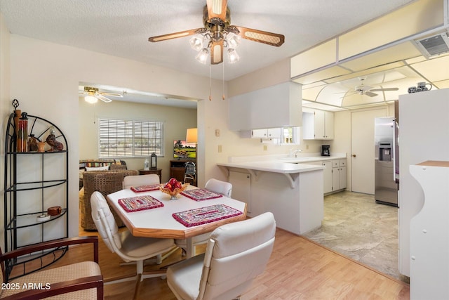 dining room with light wood-style flooring, a textured ceiling, visible vents, and a ceiling fan