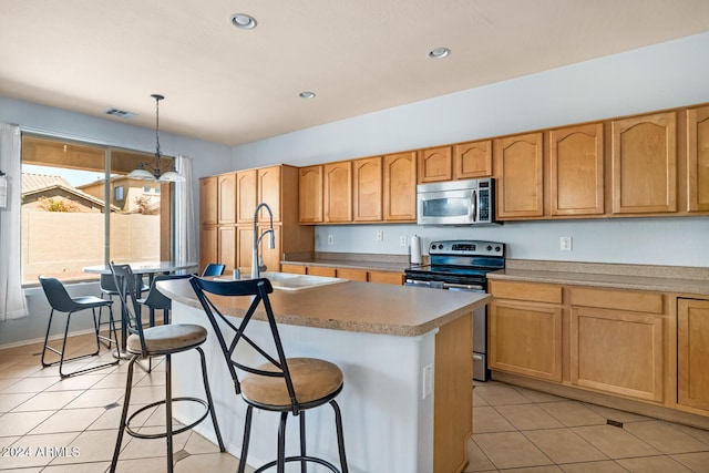 kitchen featuring light tile patterned floors, decorative light fixtures, stainless steel appliances, sink, and a center island with sink