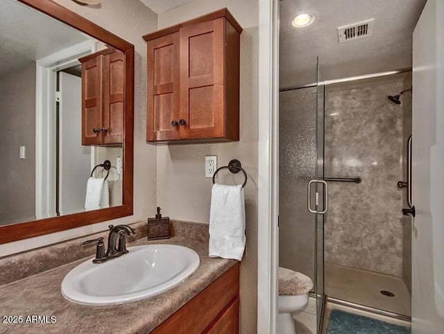 bathroom with vanity, toilet, visible vents, and a shower stall