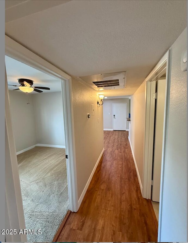 hallway featuring baseboards, a textured ceiling, and wood finished floors