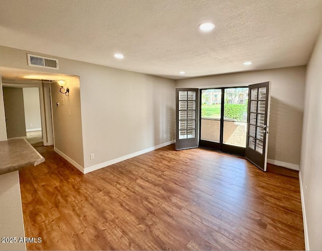 spare room featuring a textured ceiling, visible vents, wood finished floors, and baseboards