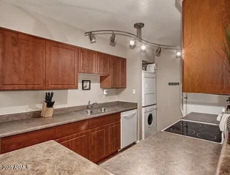 kitchen featuring brown cabinets, stacked washer and clothes dryer, a sink, and dishwasher