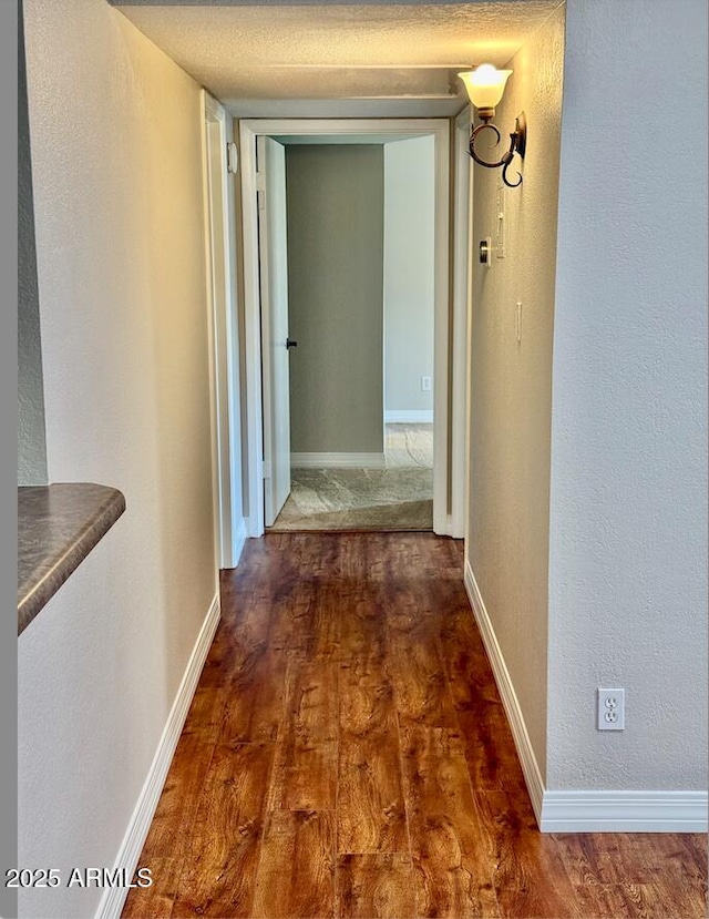 corridor with baseboards, a textured wall, and dark wood-type flooring
