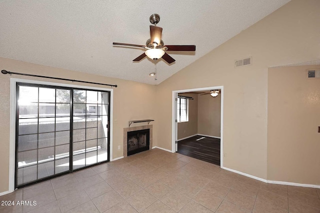 unfurnished living room featuring vaulted ceiling, a textured ceiling, light tile patterned floors, ceiling fan, and a tiled fireplace