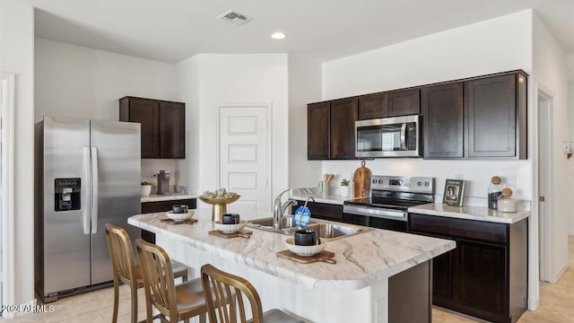 kitchen featuring appliances with stainless steel finishes, sink, a kitchen bar, a kitchen island with sink, and dark brown cabinetry