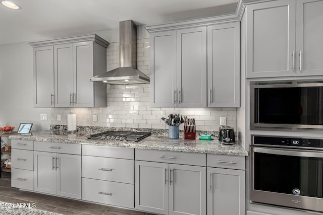 kitchen featuring light stone countertops, backsplash, appliances with stainless steel finishes, and wall chimney exhaust hood