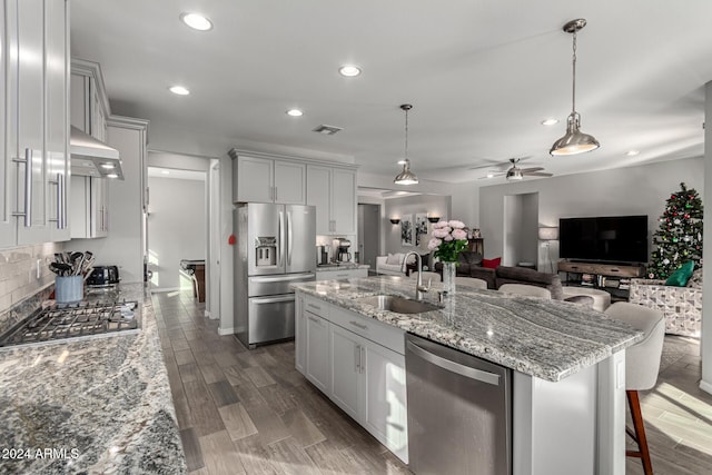 kitchen featuring light stone countertops, appliances with stainless steel finishes, decorative light fixtures, an island with sink, and sink