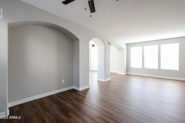 empty room with a ceiling fan, arched walkways, dark wood finished floors, and baseboards