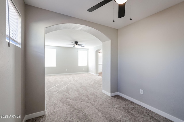 unfurnished room with a ceiling fan, arched walkways, carpet flooring, and baseboards