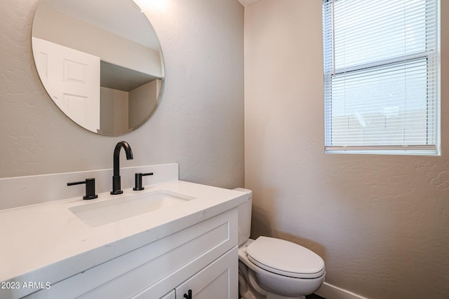 bathroom with a textured wall, vanity, and toilet