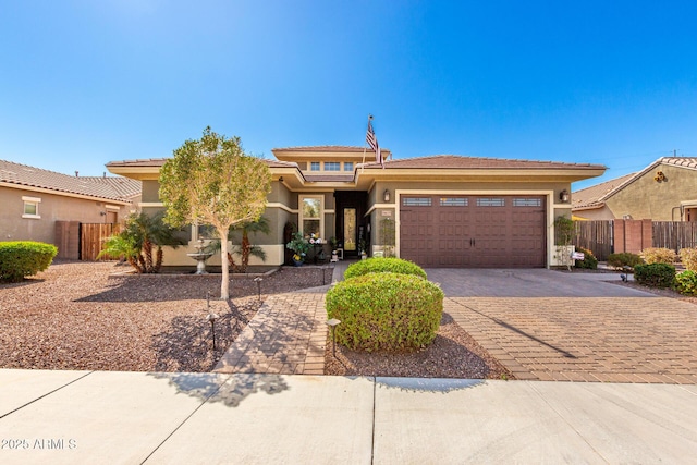 prairie-style home featuring a garage, decorative driveway, fence, and stucco siding