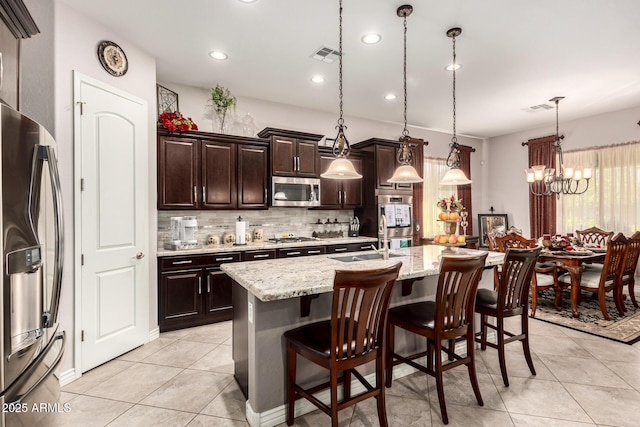 kitchen with stainless steel appliances, visible vents, a center island with sink, and a kitchen breakfast bar