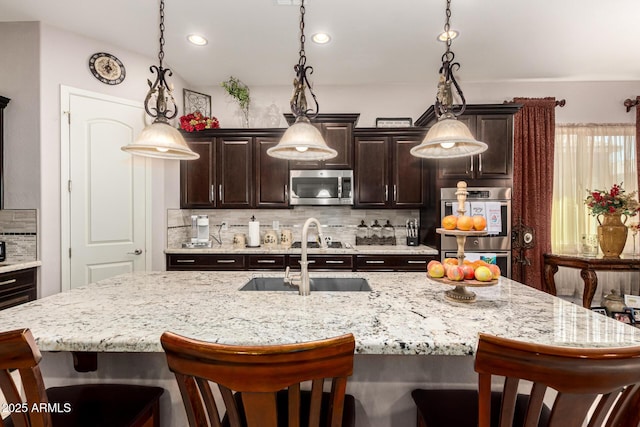 kitchen featuring a breakfast bar area, stainless steel appliances, hanging light fixtures, backsplash, and a sink