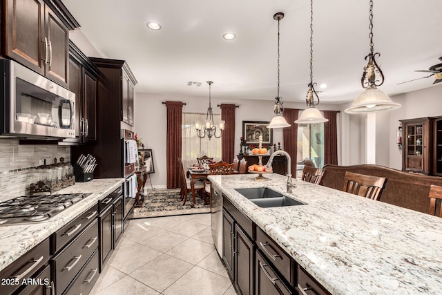 kitchen with tasteful backsplash, light stone countertops, stainless steel appliances, pendant lighting, and a sink