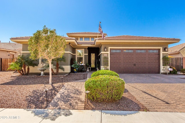 prairie-style home featuring decorative driveway, fence, an attached garage, and stucco siding