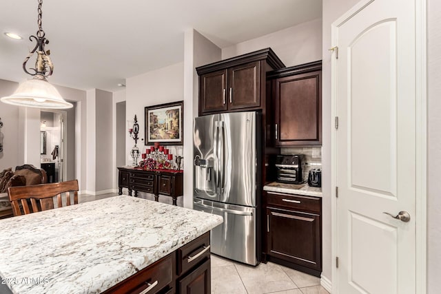 kitchen with light stone counters, light tile patterned floors, hanging light fixtures, dark brown cabinetry, and stainless steel fridge