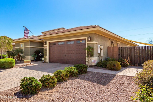 view of front of property featuring an attached garage, fence, decorative driveway, and stucco siding