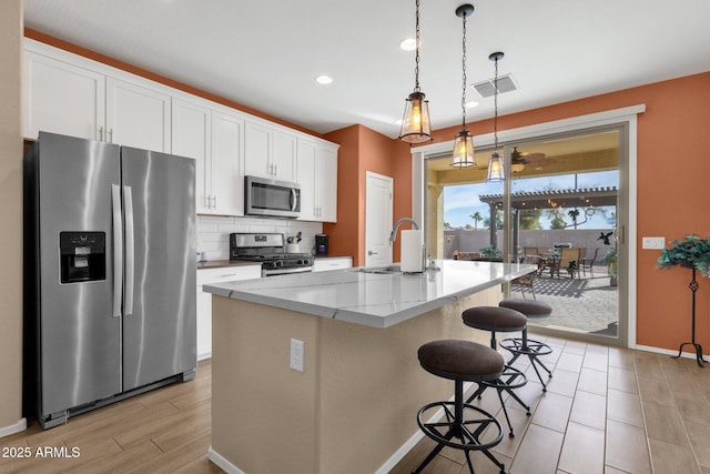 kitchen with sink, light stone counters, stainless steel appliances, a kitchen island with sink, and white cabinets