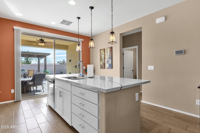 kitchen with a kitchen island with sink, light stone countertops, stainless steel dishwasher, and white cabinets