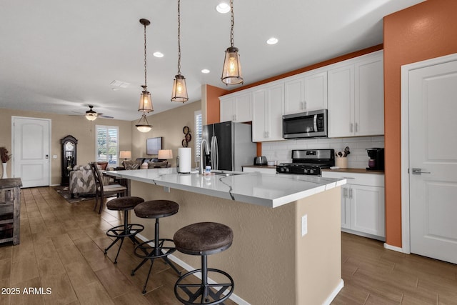 kitchen featuring appliances with stainless steel finishes, a breakfast bar, decorative light fixtures, white cabinets, and a center island with sink