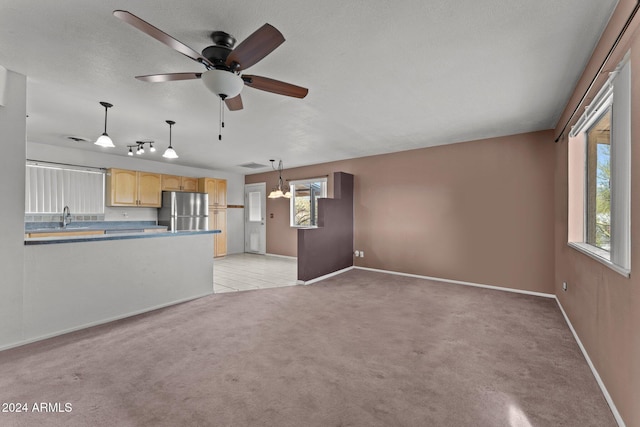 unfurnished living room with light carpet, sink, and ceiling fan with notable chandelier