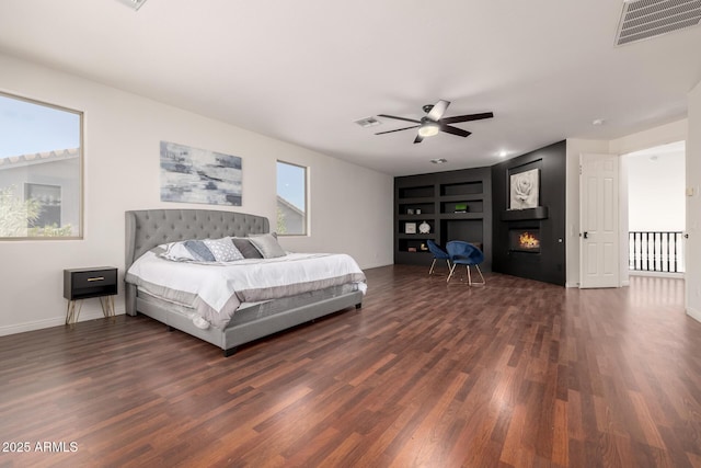 bedroom with ceiling fan, dark hardwood / wood-style floors, and a large fireplace