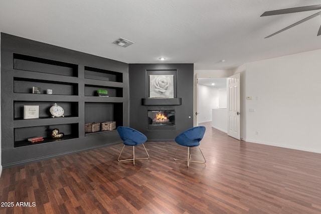 living area featuring ceiling fan, built in shelves, and dark hardwood / wood-style floors