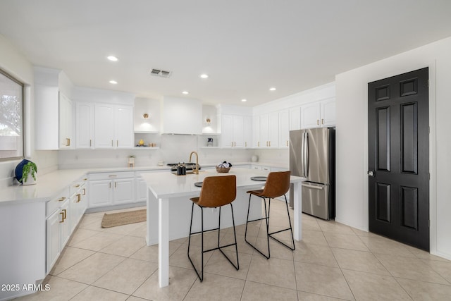 kitchen featuring white cabinets, a kitchen bar, light tile patterned floors, stainless steel refrigerator, and a kitchen island with sink