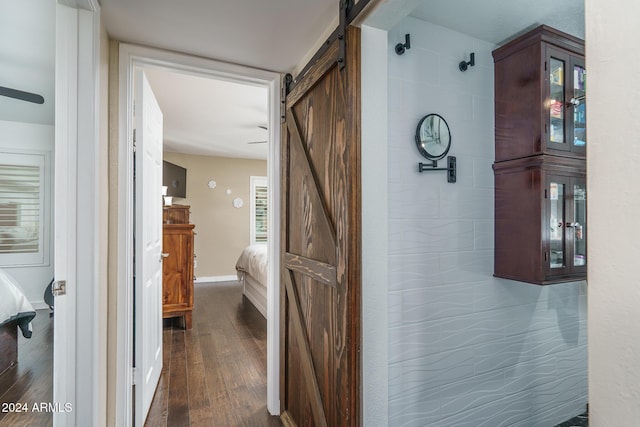 hallway featuring a barn door, baseboards, and dark wood-style flooring