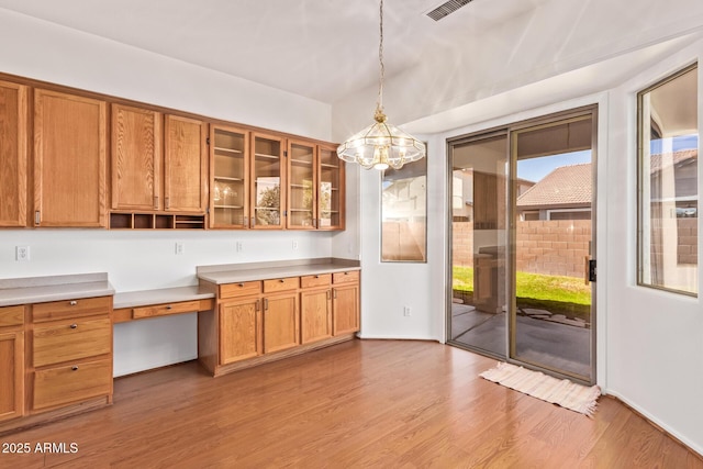 interior space with hanging light fixtures, brown cabinetry, wood finished floors, and visible vents