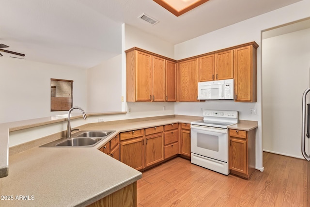 kitchen featuring visible vents, a sink, light countertops, light wood finished floors, and white appliances