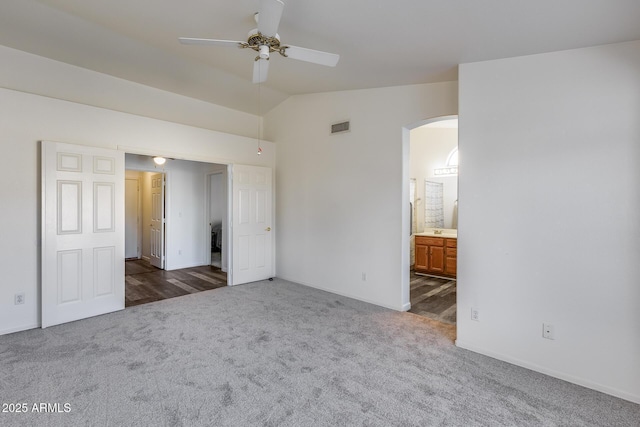 unfurnished bedroom with visible vents, arched walkways, lofted ceiling, ensuite bathroom, and carpet