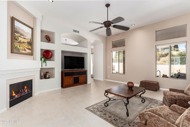 living room with ceiling fan, built in shelves, a fireplace, and light tile patterned flooring