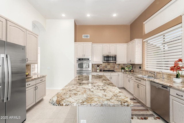 kitchen with light tile patterned floors, stainless steel appliances, sink, light stone counters, and a center island