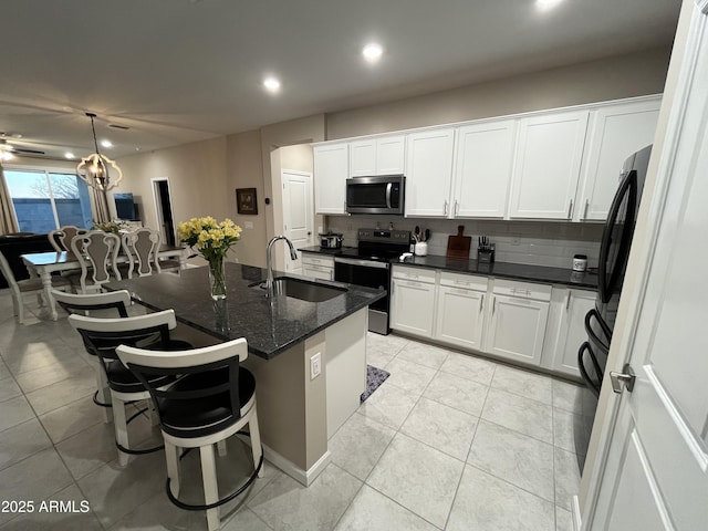 kitchen with stainless steel appliances, white cabinetry, a kitchen island with sink, and decorative backsplash