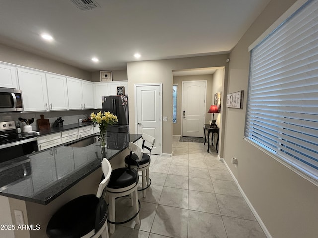 kitchen featuring sink, a breakfast bar, white cabinetry, stainless steel appliances, and dark stone counters