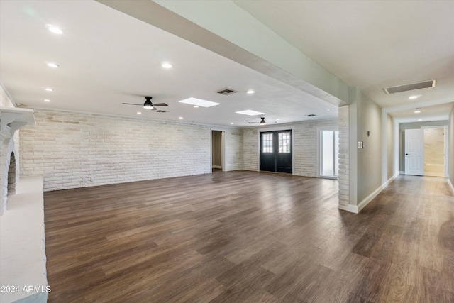 unfurnished living room with brick wall, dark hardwood / wood-style floors, a large fireplace, and ceiling fan