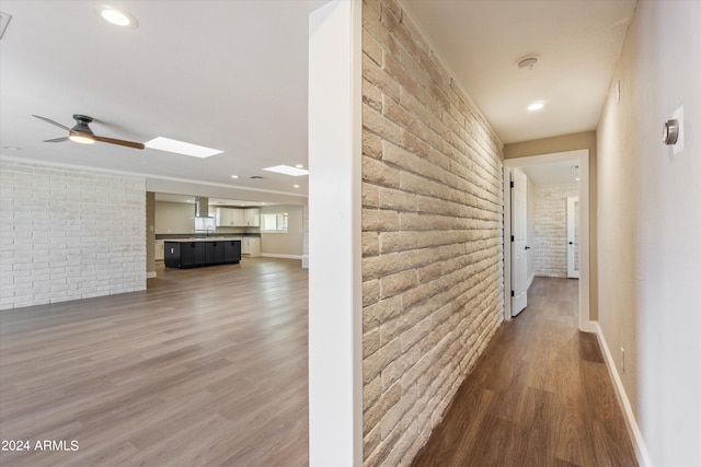 hallway featuring brick wall, wood-type flooring, and a skylight