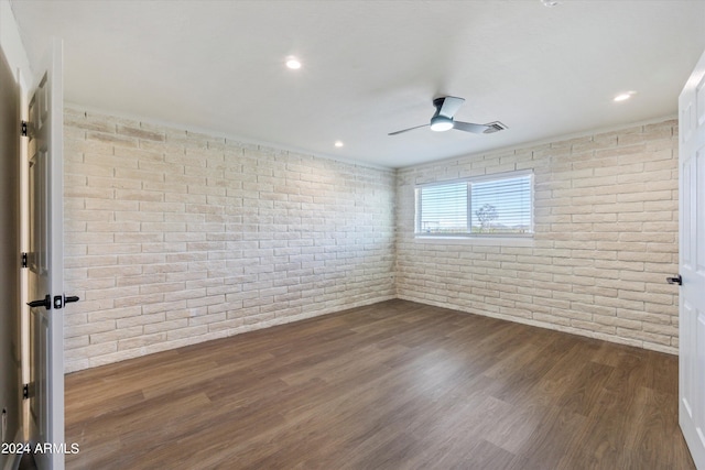 empty room featuring dark wood-type flooring, ceiling fan, and brick wall