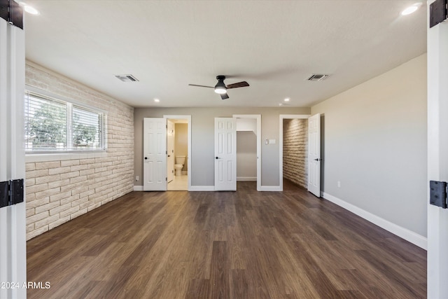 unfurnished bedroom with connected bathroom, dark wood-type flooring, brick wall, and ceiling fan