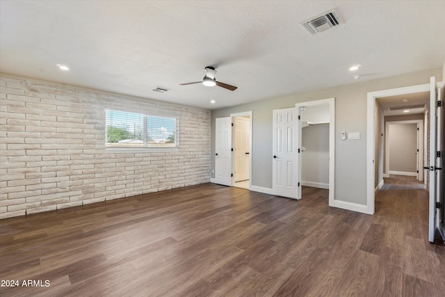 unfurnished bedroom with ceiling fan, dark hardwood / wood-style flooring, a spacious closet, a closet, and brick wall