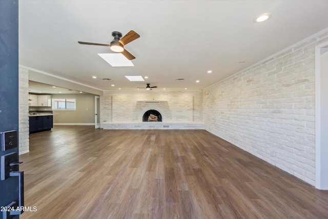 unfurnished living room featuring hardwood / wood-style floors, a large fireplace, ceiling fan, a skylight, and brick wall